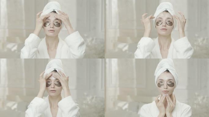 年轻女子在镜子里看着自己，穿着浴袍，用毛巾用手在脸上涂上保湿霜。