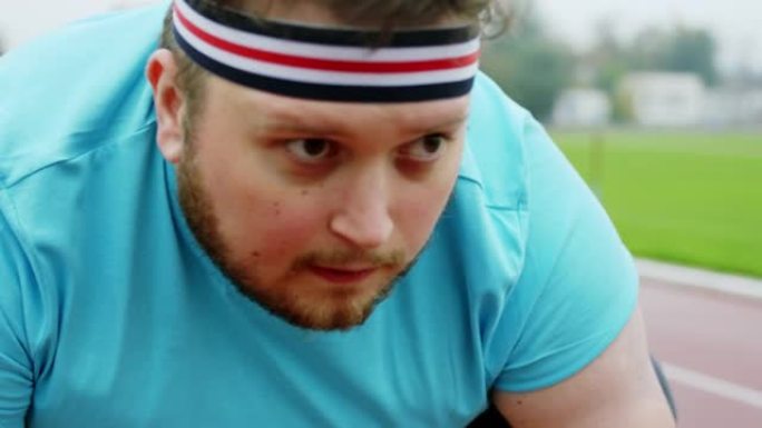 在镜头前特写镜头，起跑线上穿着运动服的肥胖家伙准备进行艰苦的锻炼