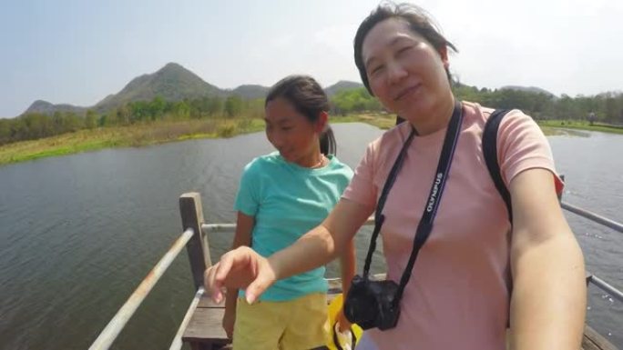 快乐的亚洲母亲和她的女儿在阳光明媚的日子里一起在湖上的桥上自拍，旅行生活方式的概念。