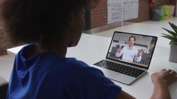 非裔美国妇女在办公室与男同事在笔记本电脑上进行视频通话的后视图