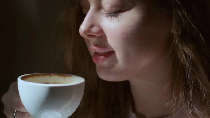 女孩从白杯中愉快地喝咖啡的特写镜头。