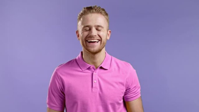 穿着粉色t恤的微笑开朗英俊男子的肖像看着镜头。盖伊在紫罗兰背景下的工作室里真诚地笑了。