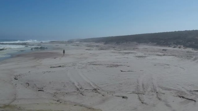阴天在薄雾笼罩的海滩上行走的妇女的脚印在沙滩上，