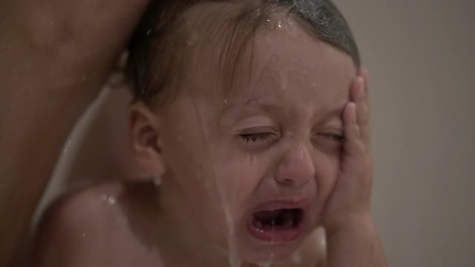 哭泣的婴儿在淋浴时洗头，洗头时眼睛发痒。心烦意乱的孩子哭泣