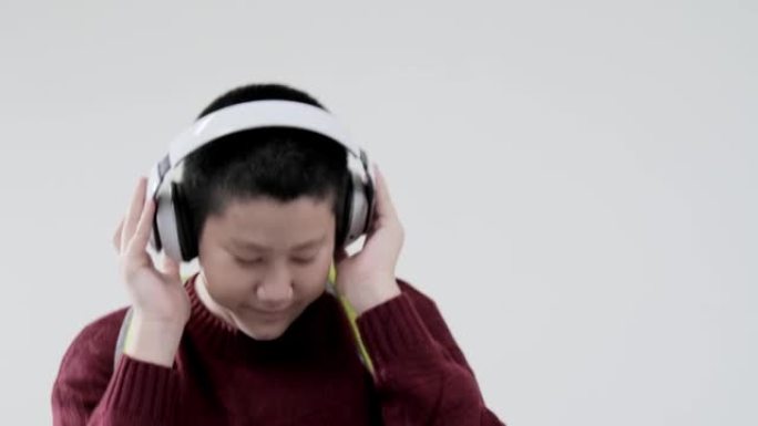 亚洲男生穿着红色毛衣跳舞唱歌，同时在灰色背景上使用无线耳机，生活方式概念。