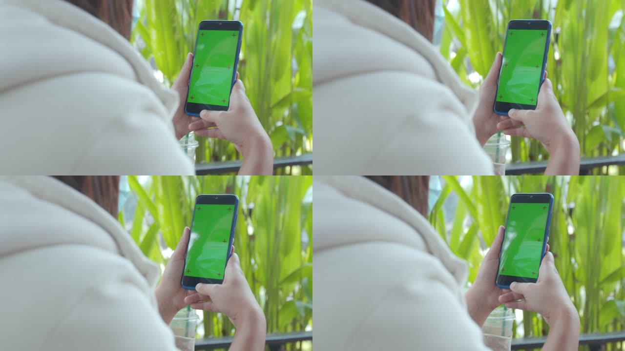 近距离拍摄的女人手持智能手机，在咖啡馆里用色度键绿色屏幕慢动作拍摄。