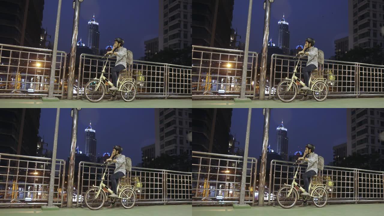亚洲商人和他的自行车在立交桥路上，并使用具有现代建筑背景的手机
