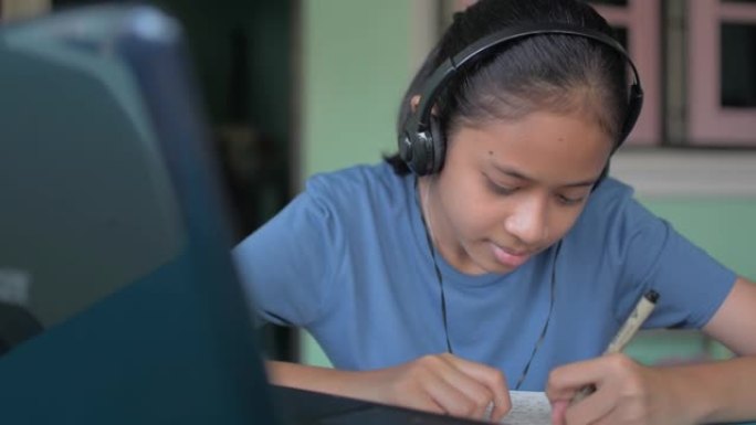 亚洲少女，穿着休闲装的泰国高中生戴着耳机看网络直播课看笔记本电脑。