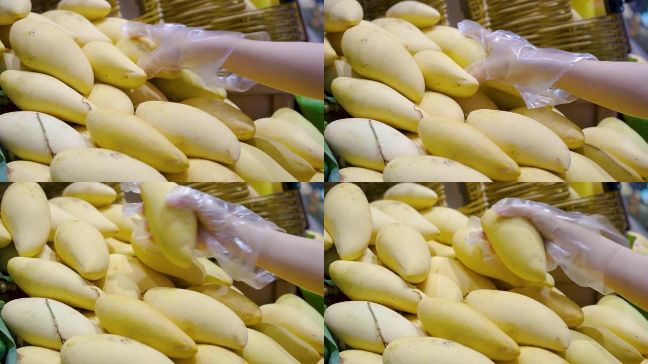 戴橡胶手套的女性手可以防止病毒在杂货店选择芒果
