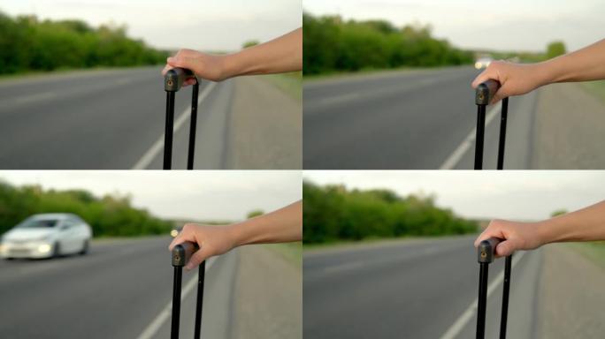 在高速公路上经过的汽车的背景下，一个女人在手提箱里拿着把手的特写镜头