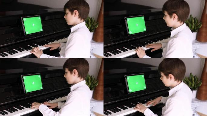 学校男孩学习弹钢琴与平板电脑应用程序。孩子喜欢学习演奏乐器。平板电脑与绿屏色度键背景新的应用程序，商