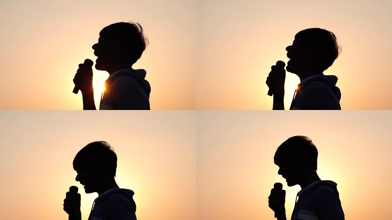 日落时，一个孩子在麦克风里对着太阳尖叫的剪影。Kid演唱摇滚歌曲并在麦克风中大喊大叫