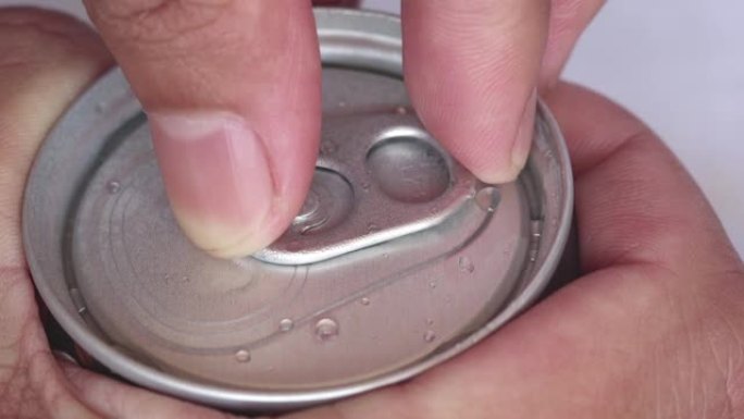 特写镜头的手正在打开铝制的咖啡罐，里面有气体，焦点灵敏。湿铝罐上的水滴。