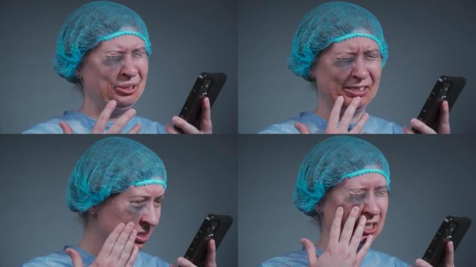 穿着一次性蓝色医用防护服的女性患者哭泣并打电话给急诊医院的保险公司。在诊所发生暴力事件后面部受伤的女