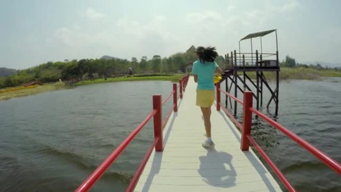 快乐的亚洲女孩在阳光明媚的日子里与家人一起在湖上的桥上奔跑，旅行生活方式的理念。