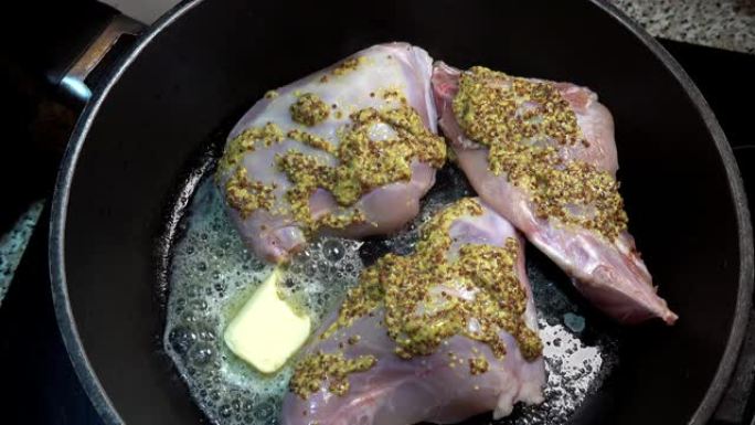 用融化的黄油将涂有粗芥末的兔子腿放入锅中