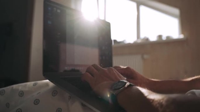 男人的手在笔记本电脑上打字美丽的阳光从窗户落下日落的阴影躺在床上，员工正在计算机上慢动作