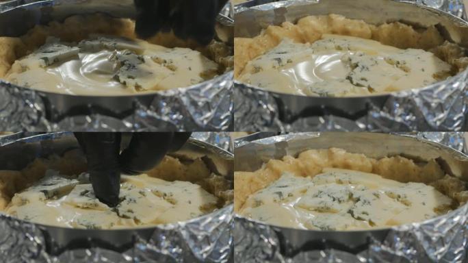 厨师在烘烤前将蓝色奶酪块放在馅饼上。奶酪给蛋糕带来持久宜人的香气。天然自制食品