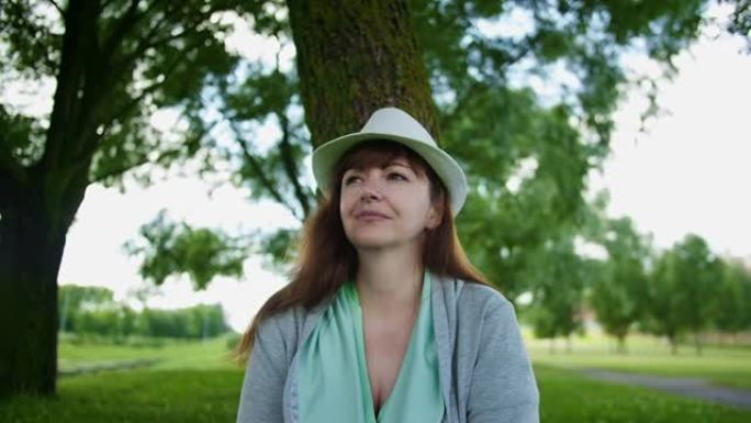 公园树附近一位戴着帽子的黑发女子看着相机的肖像