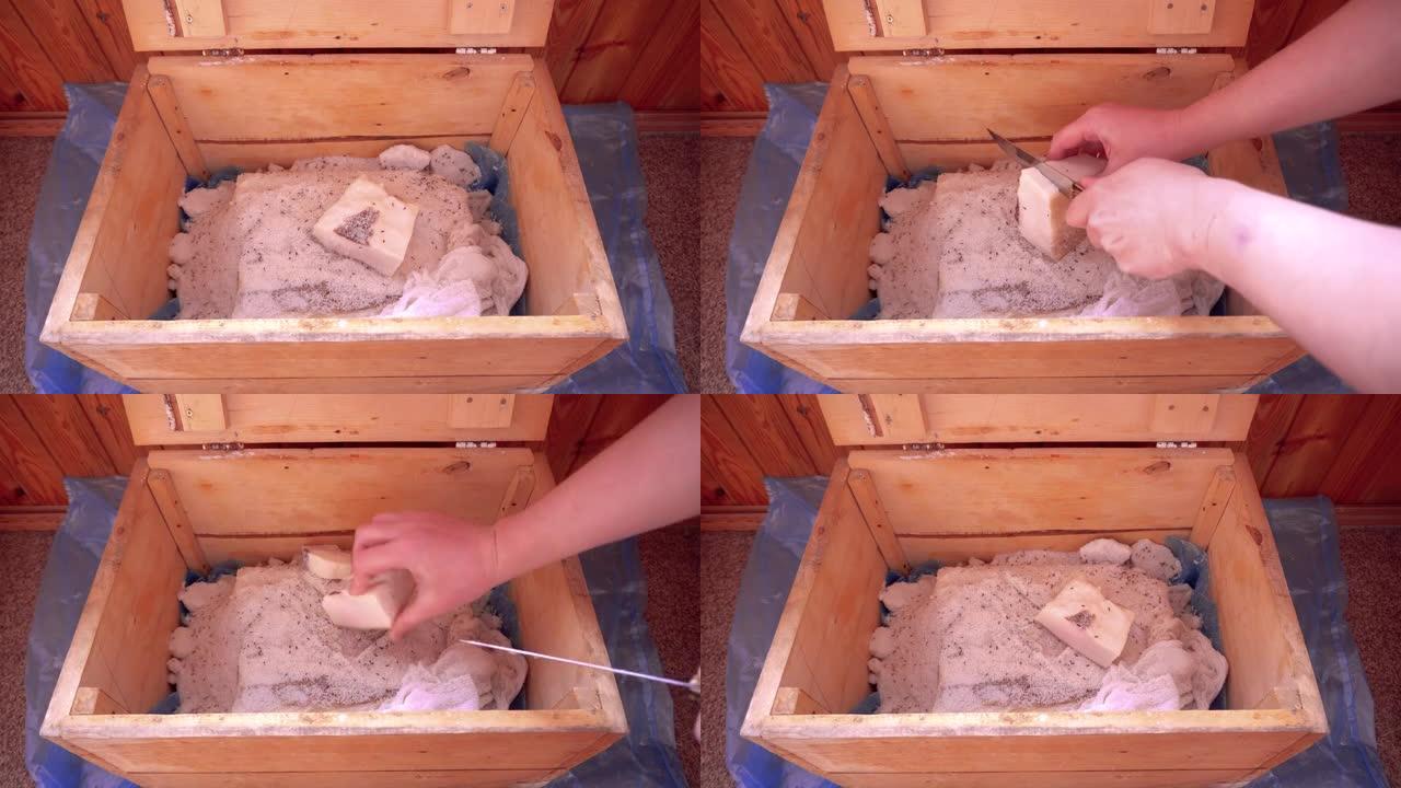 一只手打开一个木箱，在其中用猪油腌制，用纱布覆盖并切下一块腌制的猪油