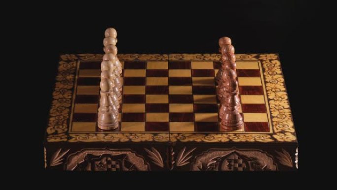 在棋盘上放置雕刻的木制棋子，延时。手工制作的棋子在黑色背景上首次亮相之前