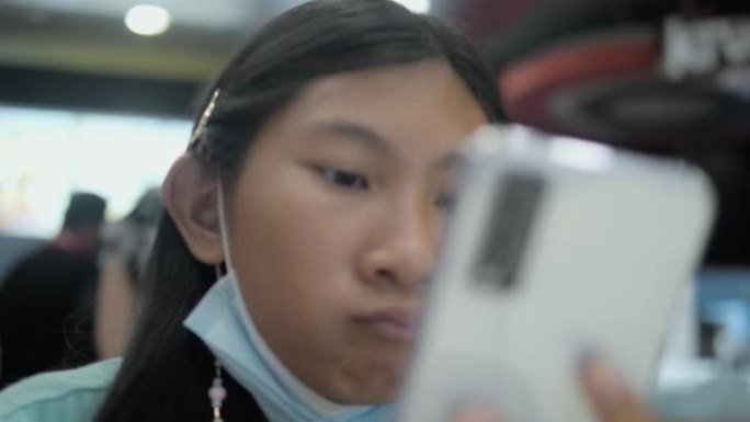 快乐的亚洲女孩在垃圾食品餐厅使用智能手机，生活方式概念。