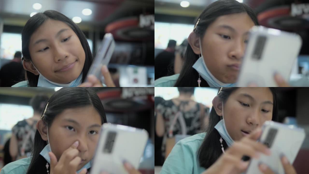 快乐的亚洲女孩在垃圾食品餐厅使用智能手机，生活方式概念。