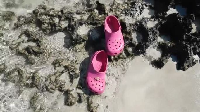 粉红色的凉鞋漂浮在沙滩上的清澈水中