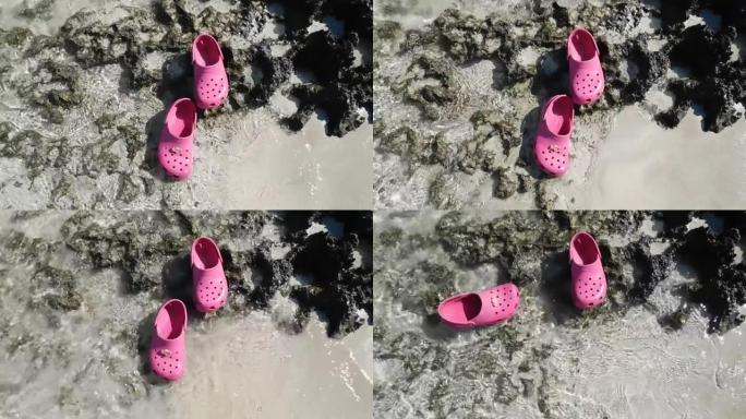 粉红色的凉鞋漂浮在沙滩上的清澈水中
