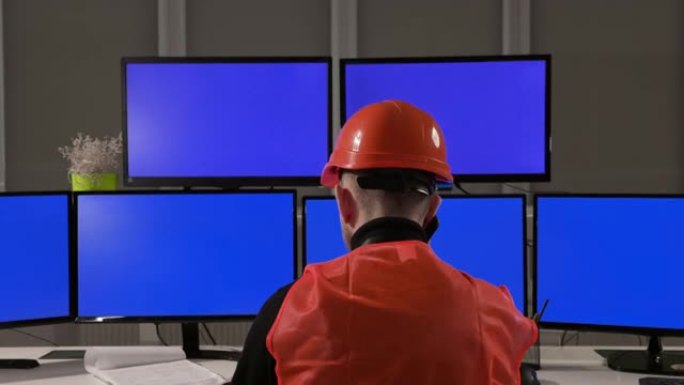 一位身穿头盔和背心的工程师坐在许多电脑屏幕前。他控制着这个过程。年轻人拿起电话接听电话。