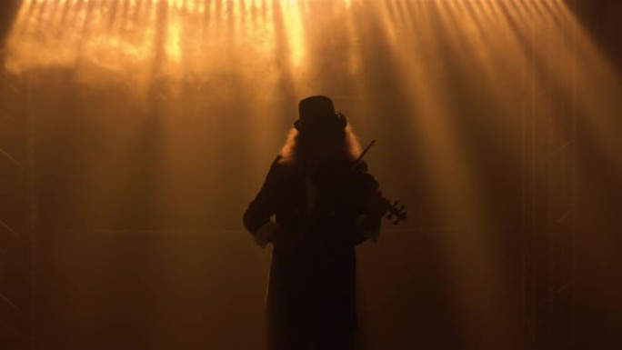 小提琴家音乐家的剪影，头发茂密，戴着帽子，演奏古典木制小提琴。一名男子在黑烟的工作室里用黄灯表演独奏