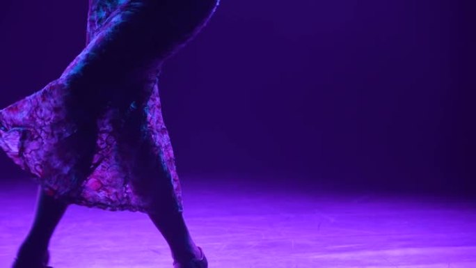 穿着蕾丝连衣裙跳舞的迷人黑发女郎的剪影，用手表演优美的动作。女人在紫色灯光的黑暗烟熏工作室里跳舞弗拉