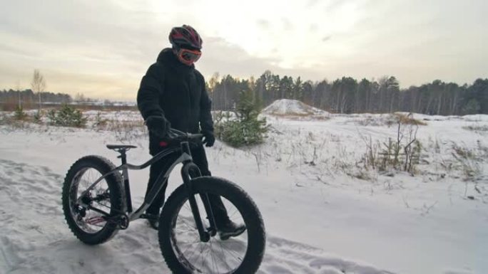 专业极限运动员骑自行车的人在户外用胖自行车行走。骑自行车的人走在冬天的雪林里。男子戴着头盔和眼镜的大