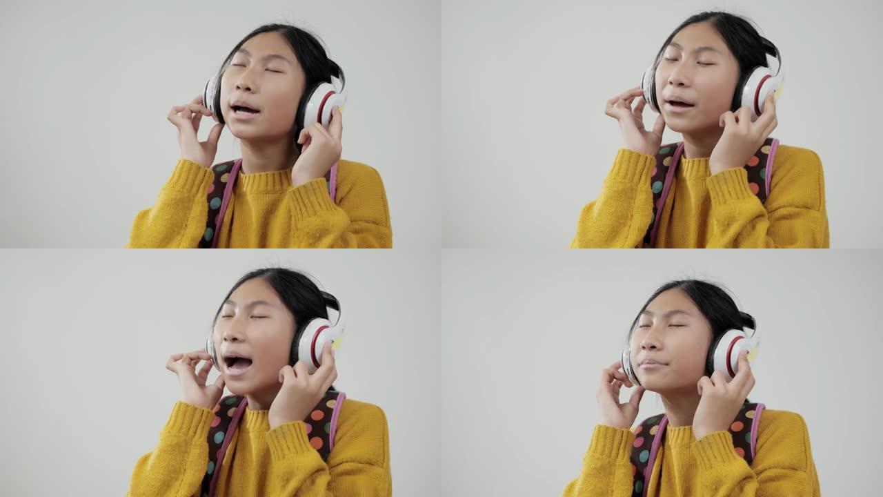 快乐的亚洲女孩使用耳机，在灰色背景下唱歌跳舞，教育生活方式理念。