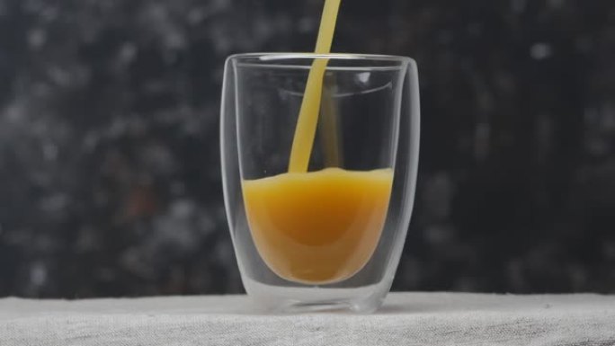 将柑橘汁倒入双层玻璃杯中。黑色背景上的玻璃特写。慢动作