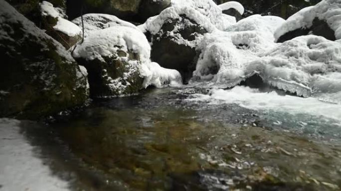 在针叶林中流淌的山区河流的死水特写。冰雪中的冰冻石头。横向移动滑动。广角