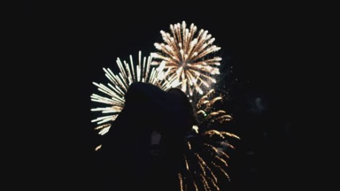 情侣晚上看烟火，仰望天空。一个年轻男孩和一个女孩在节日里五颜六色的烟花背景下跳舞的剪影。活动和假期的