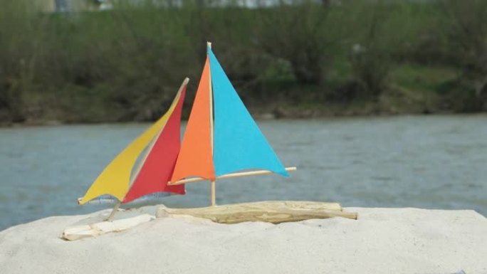 自制玩具帆船在山河背景上的沙滩上