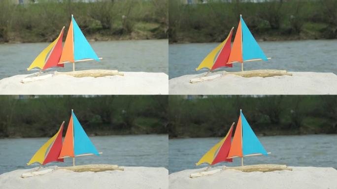 自制玩具帆船在山河背景上的沙滩上