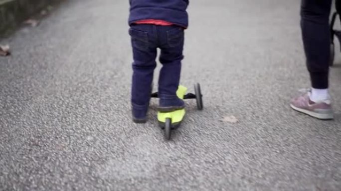 蹒跚学步的孩子在公园骑三轮玩具踏板车