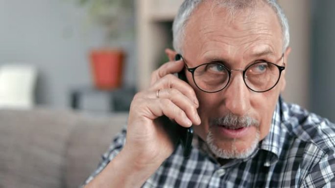 特写镜头面对70年代的老人正在说话的智能手机打电话给坐在家里沙发上的医生诊所