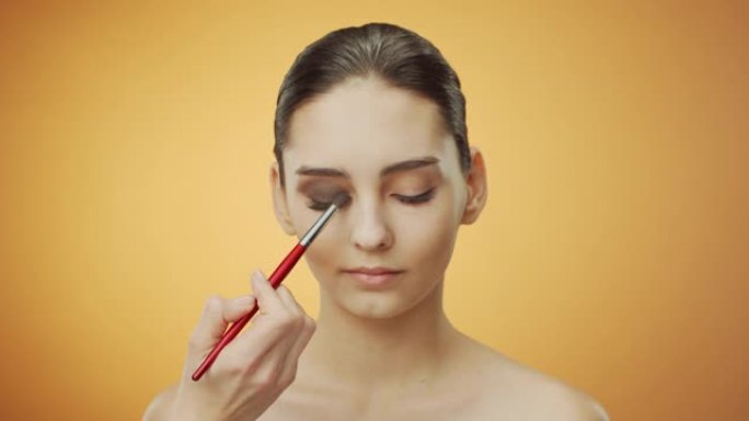 化妆申请的步骤。化妆师在一个黑发女孩闭合的眼睑上遮住棕色阴影。