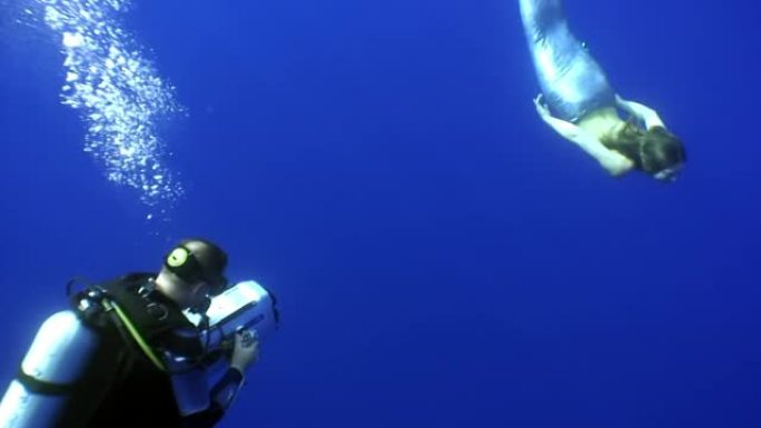 摄影师在大海中干净的蓝色背景下拍摄水下美人鱼。