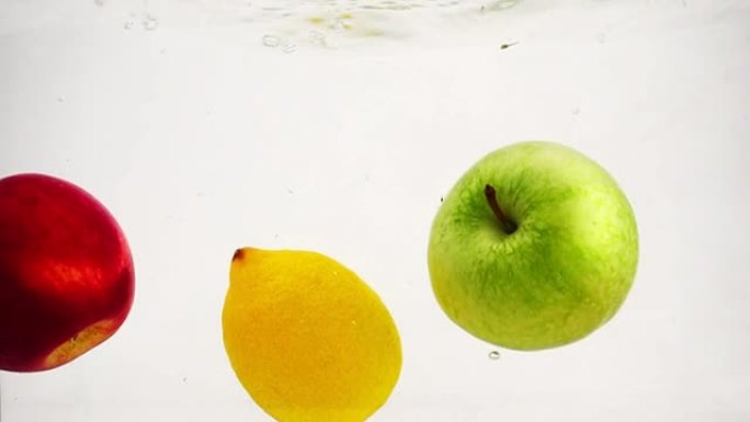 苹果，柠檬和橙子美丽地落入水中，并带有气泡。摄录在慢动作中的果实。