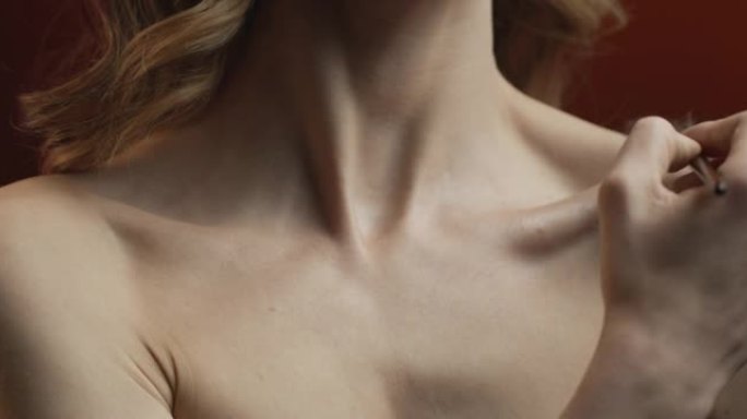 身体锁骨的特写镜头，一名妇女用化妆刷将荧光笔风扇涂在其上。