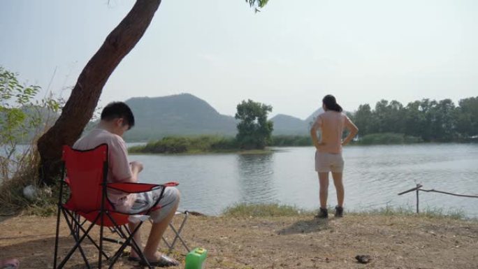 亚洲家庭在阳光明媚的日子里用红色野营椅放松附近的湖，生活方式的概念。