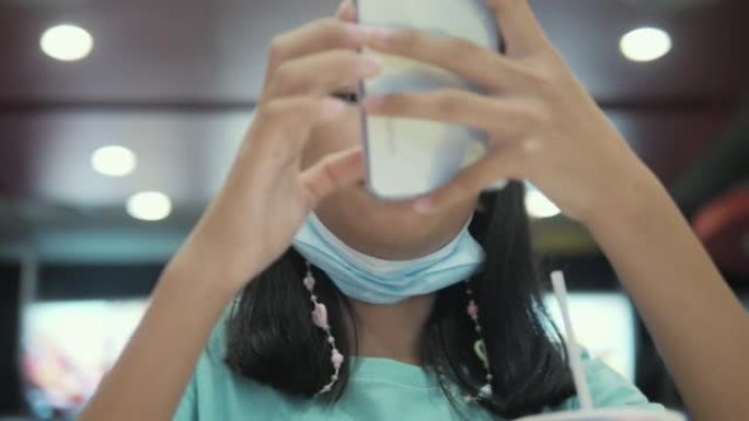快乐的亚洲女孩坐在垃圾食品餐厅，生活方式概念，通过智能手机观看病毒视频。