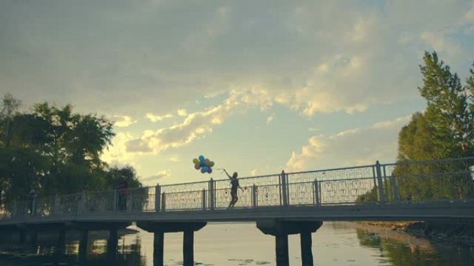 一个年轻女孩从长桥上跑下来，手里拿着彩色气球。慢动作