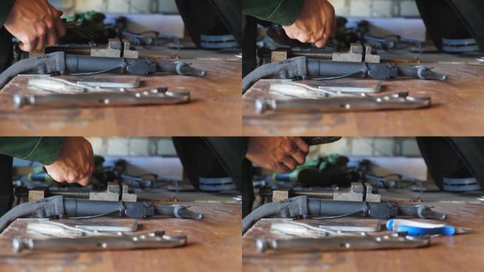 在车间用钳子将金属细节固定在桌子上的修理工的男性手。在车库工作的年轻机械师。维护服务的概念。关闭慢动