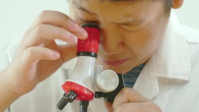 亚洲男生穿着实验服在科学课上使用显微镜，教育理念。